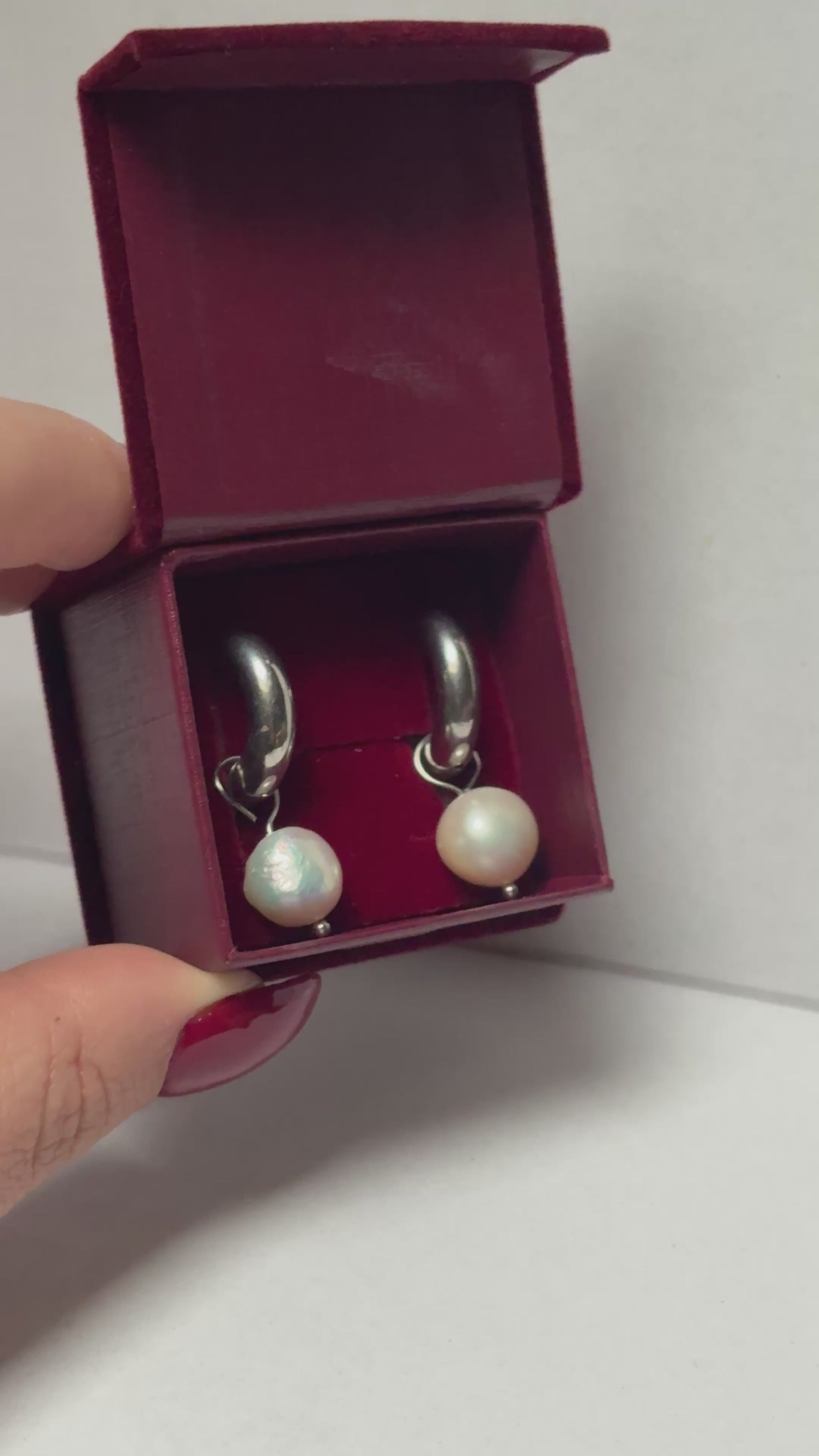 Open jewelry box with pearl earrings held by a hand on a light gray background